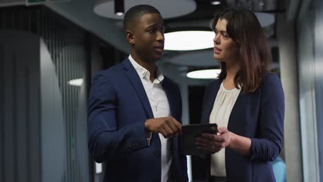 Diverse-businessman-and-businesswoman-talking-and-using-tablet-in-modern-office