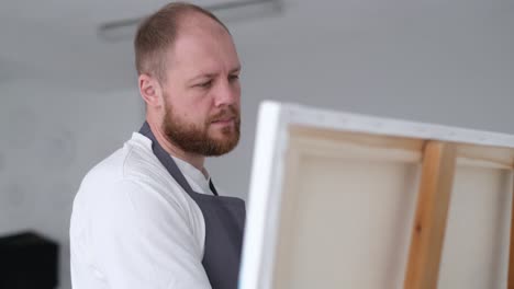 a young artist sits at home on a stool in front of a canvas and works with inspiration paints a