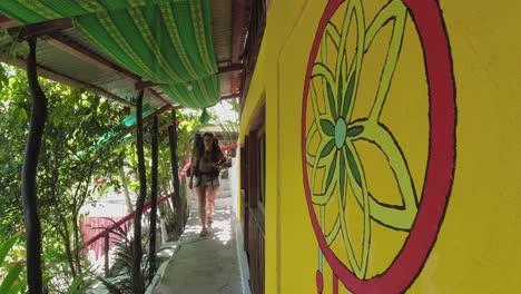 young latin female backpacker walks along bright jungle hostel hallway