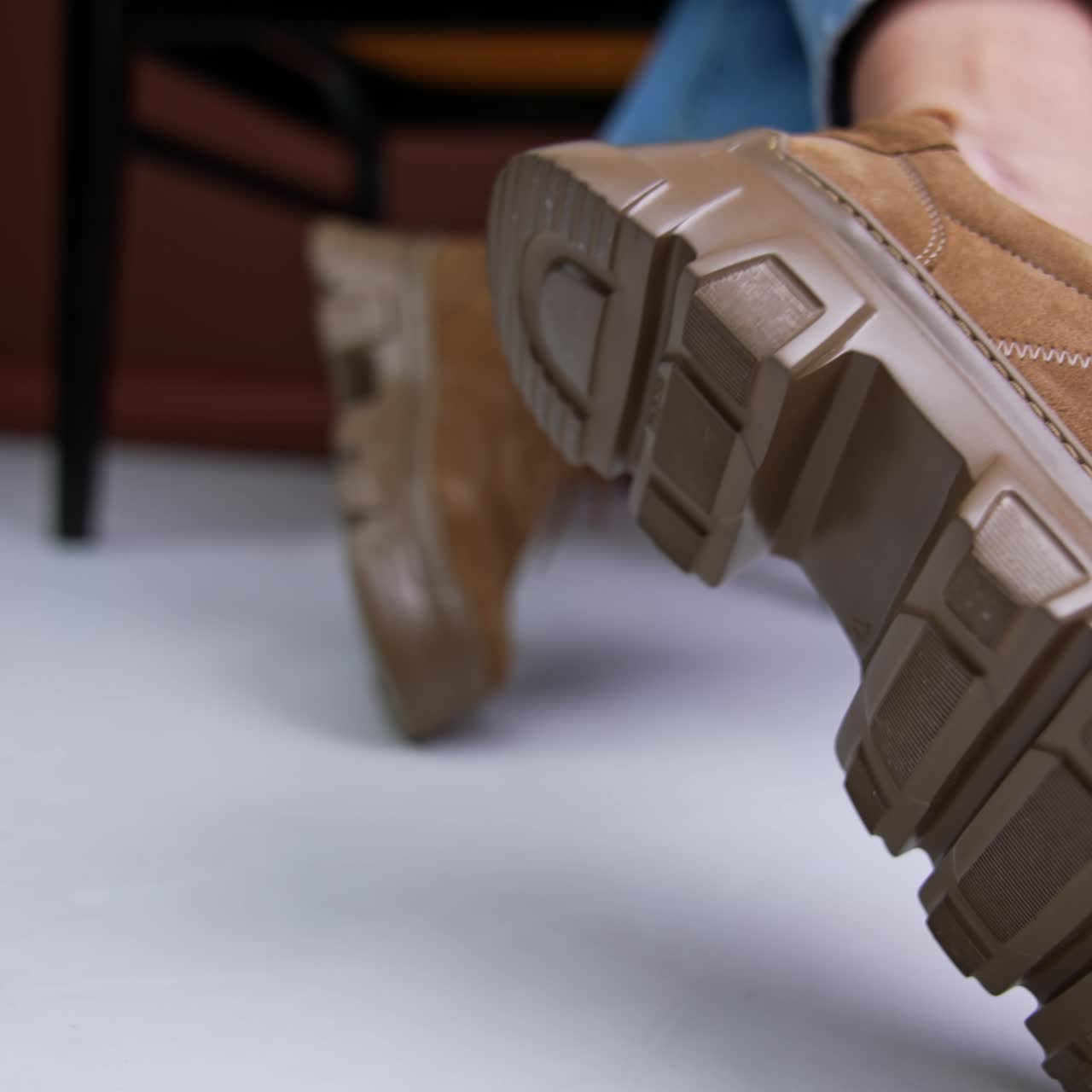 Beautiful brown stylish suede shoes on massive tractor soles. Model sitting on chair demonstrating her fashionable boots. Close up. Blurred backdrop