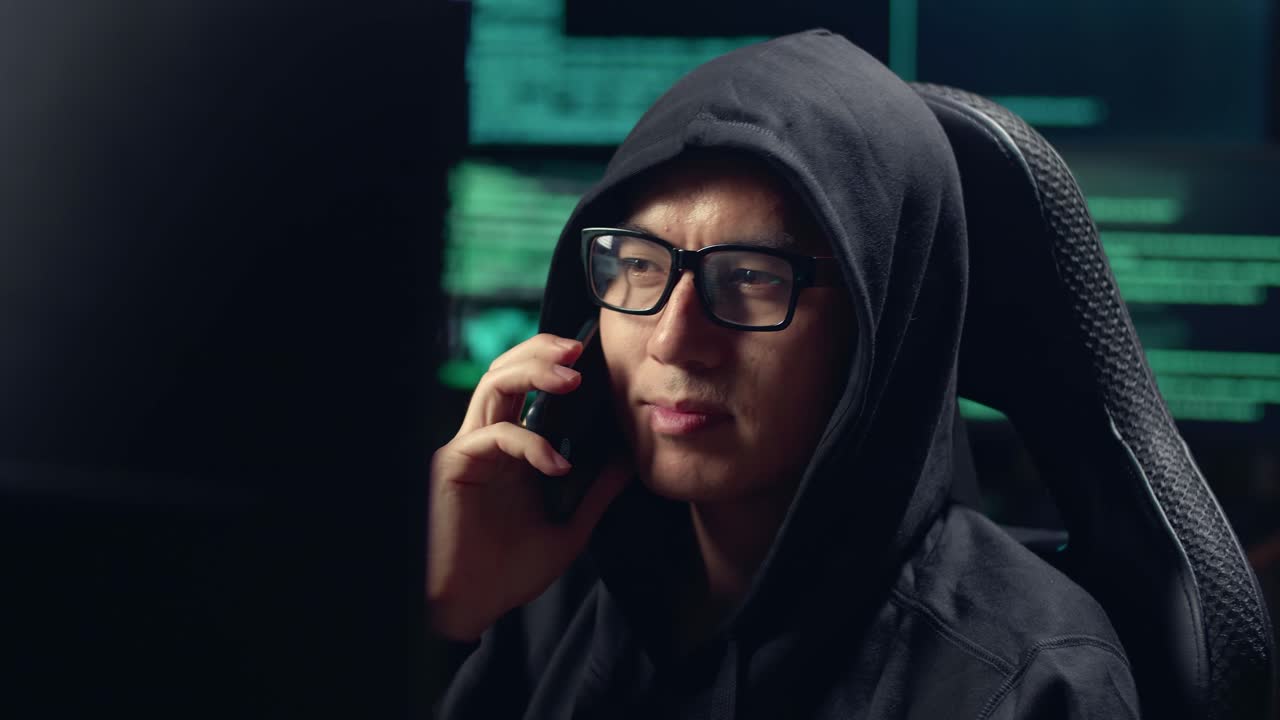 Hacker asiatico uomo che hackera al computer e parla al telefono