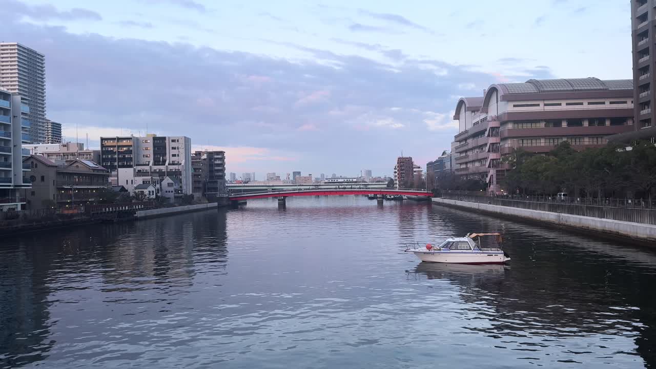 A small boat floats on a calm river in Harumi, Tokyo, with a red bridge in view