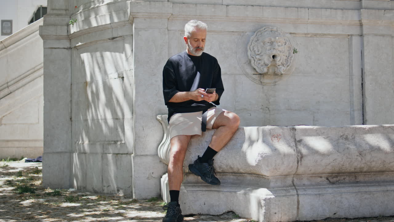 수염이 있는 여행자가 휴대전화로 문자를 입력하고 성숙한 남자가 문자 메시지를 보내고 있다.