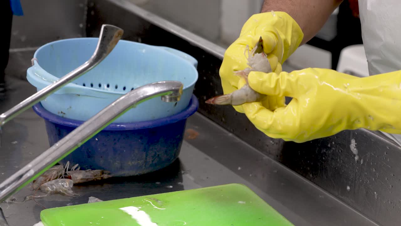 Hands clad in yellow gloves skillfully clean and chop vibrant vegetables in a lively kitchen. Fresh produce gleams as water flows