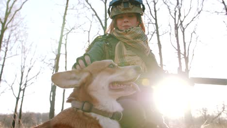 young pretty redhead woman in military uniform armed with rifle playing with dog