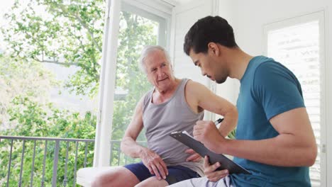 Caucasian-senior-man-explaining-while-biracial-male-instructor-making-a-note-on-clipboard