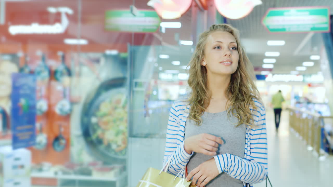 joven feliz con bolsas de compras va a lo largo de los escaparates del centro comercial video hd