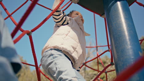 child climbing net at playground sunny day closeup. cute girl having fun