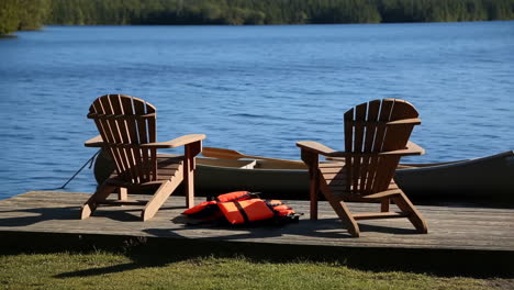 two adirondack chairs on a dock by a lake with a canoe and life jackets