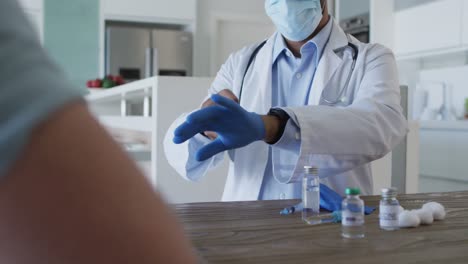 médico de raça mista usando máscara preparando vacina para paciente do sexo masculino em casa