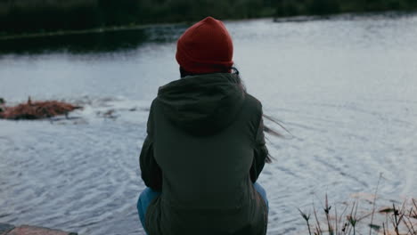 Mujer-Joven-Solitaria-Sentada-En-El-Parque-Disfrutando-De-Un-Tranquilo-Estanque-Natural-Adolescente-Sintiéndose-Deprimida-En-Un-Día-Nublado-El-Viento-Soplando-El-Pelo