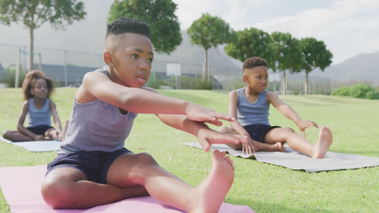 video de tres escolares afroamericanos practicando yoga sentados en una clase al aire libre