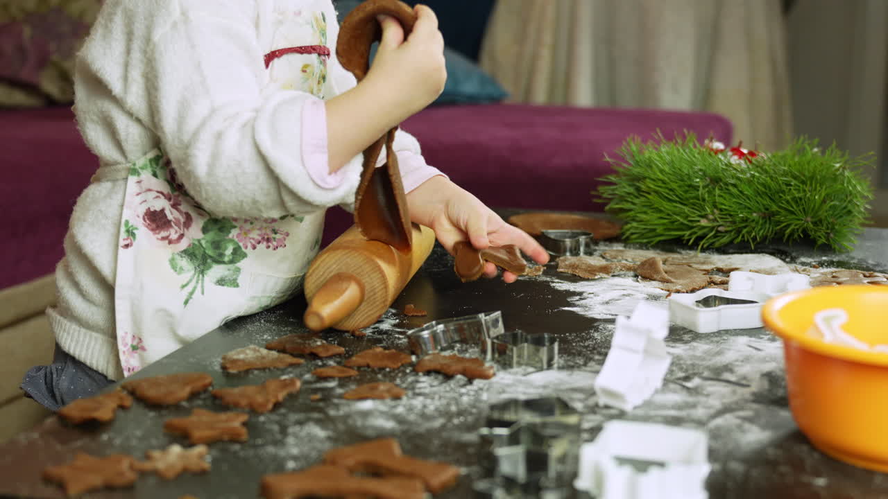 niña haciendo galletas de pan de jengibre para navidad usando un rodillo y varios cortadores de galletas en casa