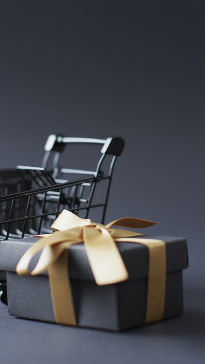 Vertical video of shopping trolley, shopping bag and gift box with copy space over grey background