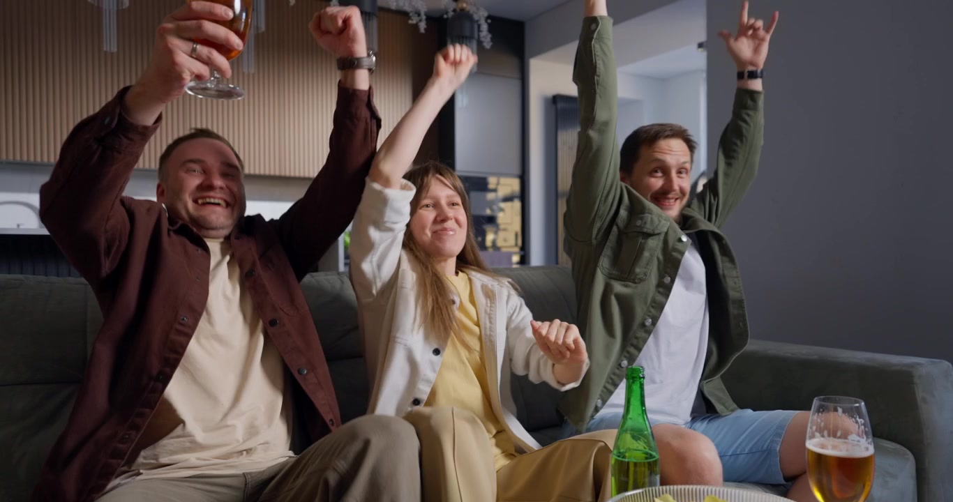 Group of Friends Cheering While Watching TV and Drinking Beer at Home