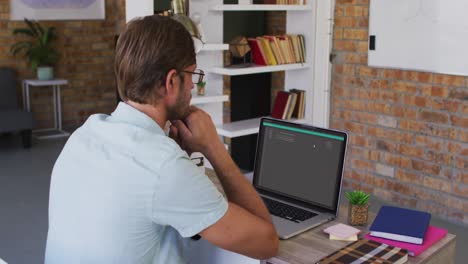 hombre caucásico sentado en el escritorio viendo el procesamiento de datos de codificación en la pantalla del portátil