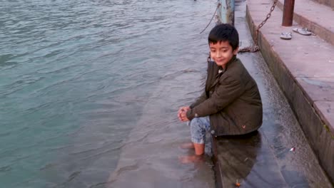 isolated-young-kid-sitting-at-the-shore-of-holy-ganges-river-bank-from-flat-angle-video-is-taken-at-ganga-river-bank-rishikesh-uttrakhand-india