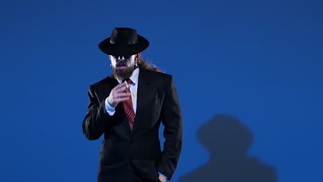 a man in a black suit and fedora with long hair and a beard against a blue background