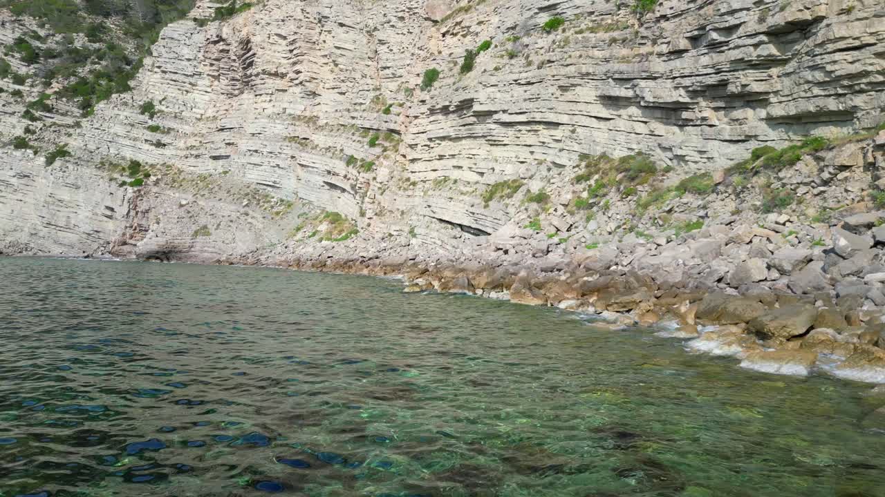 Transparent turquoise water flows between rocks in a bay in Ibiza, Spain. Beautiful aerial view flight dolly right drone
