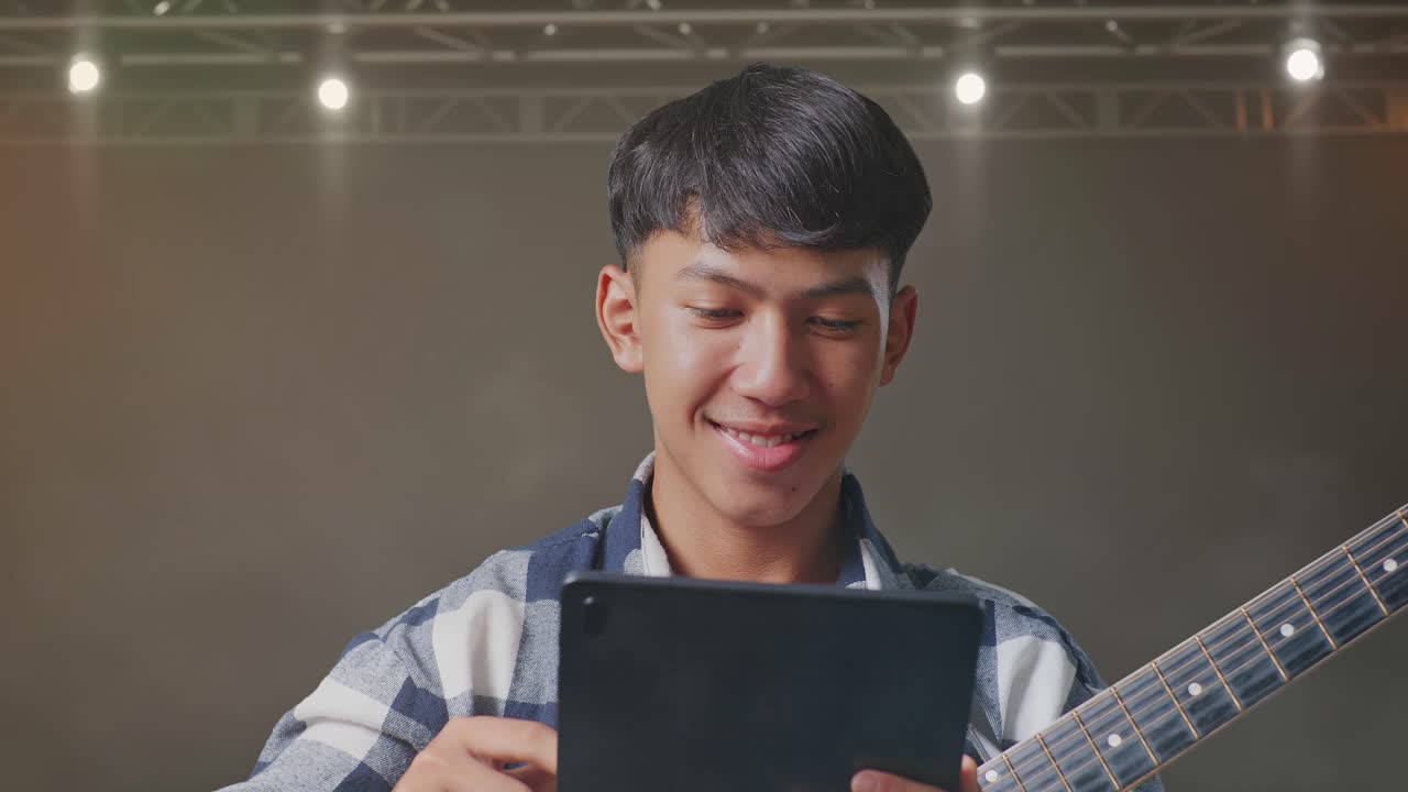무대에서 서 있는 태블릿을 사용하여 기타를 연주하는 아시아 십대의 클로즈업
