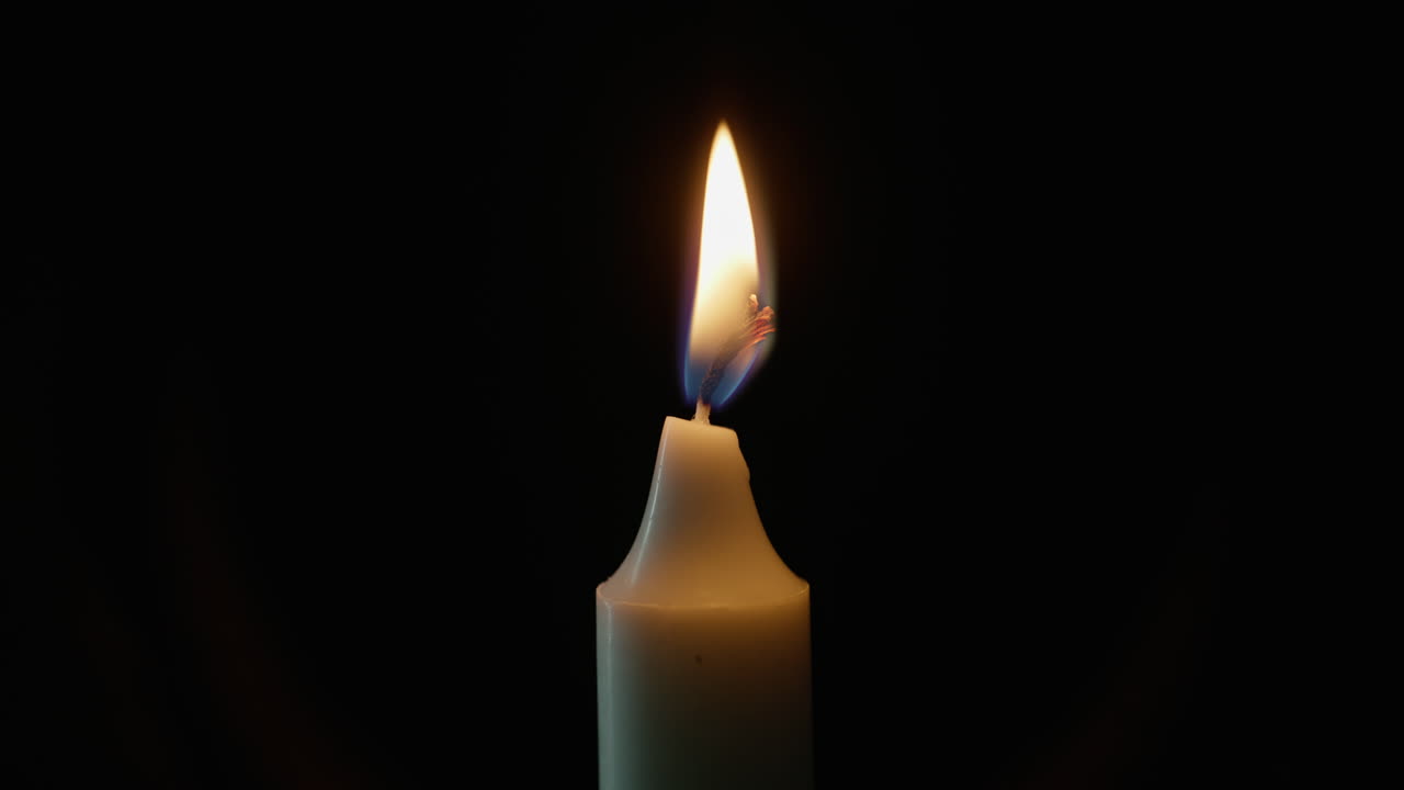 Gros plan d’une bougie de cire allumée sur fond sombre.
