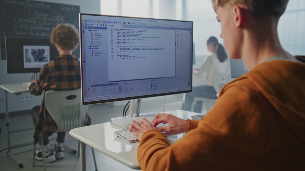 Concentrated Student in Orange Hoodie Writes Code for Video Game on Computer