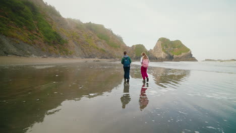 two backpackers walk along a serene coastal beach with cliffs and sea stacks
