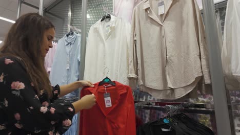 woman browsing shirts in a clothing store, inspecting clothes under soft lighting