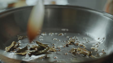 close-up of stirring indian spices in hot oil in frying pan with spatula