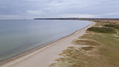 Toma-Aérea-Sobre-Una-Playa-Con-Una-Bandada-De-Pájaros-Volando-En-Rewa,-Polonia