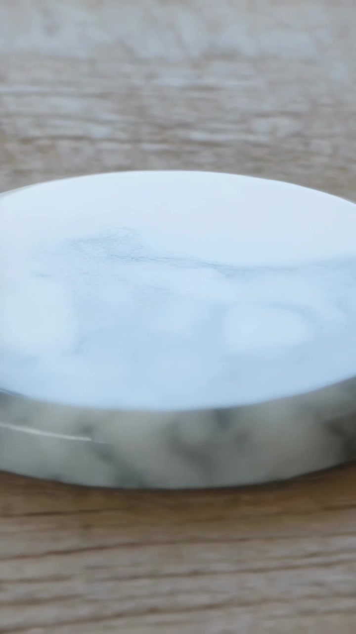 Video verticale: Telecamera che panoramica mostrando un sottobicchiere di marmo su un tavolo di legno, rivelando venature grigie per un annuncio.
