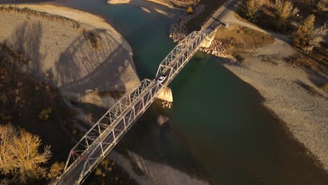 4k drone showcasing an old truss bridge near pincher creek in southern Alberta on a sunny autumn morning. Aerial orbit around the steel structure that crosses old man river within golden brown forest