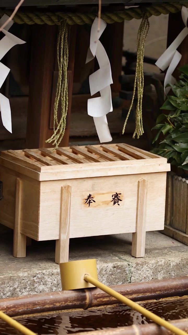 Imagem estática de uma caixa de oferendas de madeira e uma concha de bambu em um santuário xintoísta