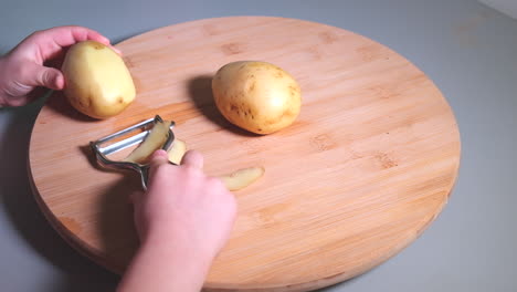 hands of little girl peeling potatoes with peeler on wooden desk, childhood and domestic help concept