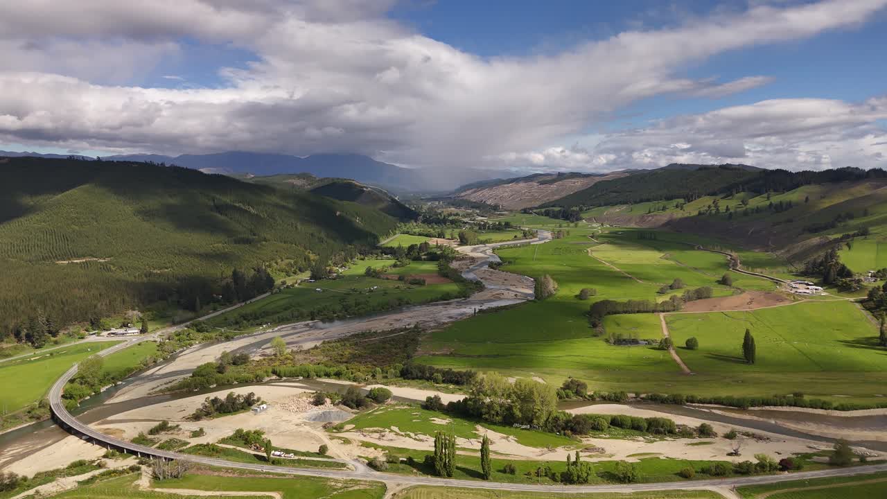 Veduta aerea del fiume Motueka che serpeggia attraverso verdi terreni agricoli nella regione di Tasman, Isola del Sud, Nuova Zelanda, con campagna rurale, dolci colline e un paesaggio agricolo scenografico sotto nuvole drammatiche
