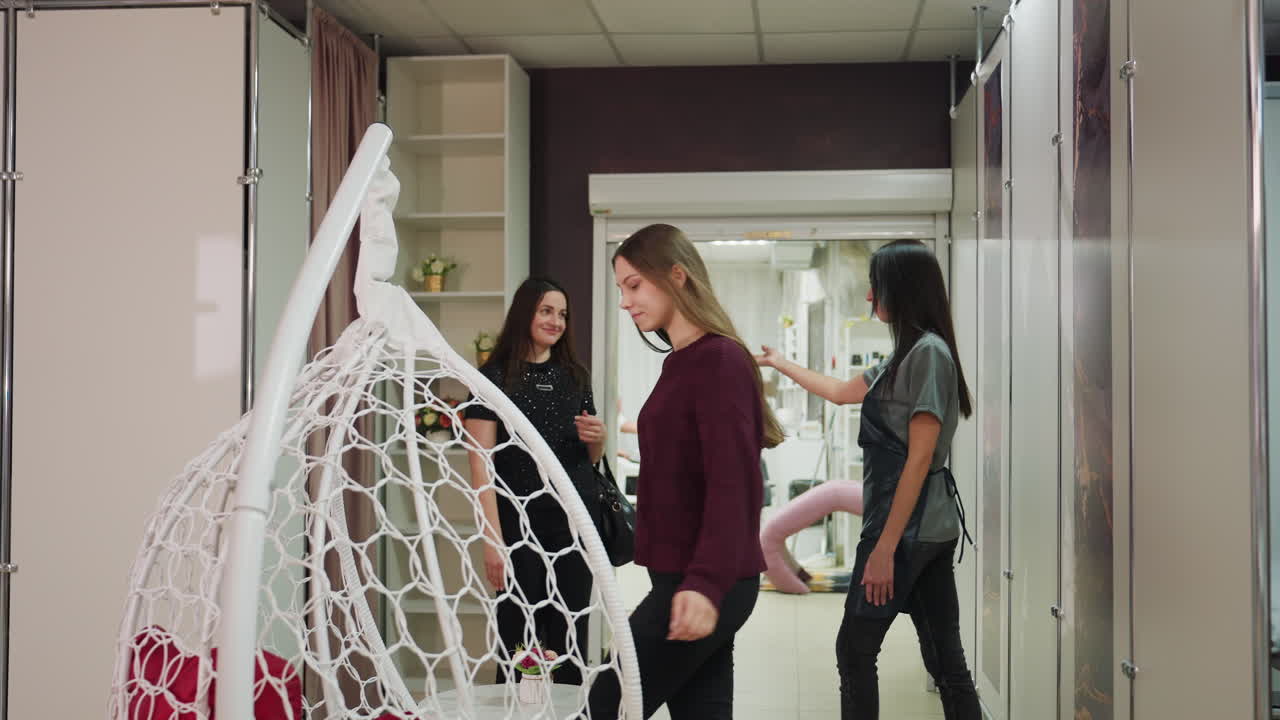 손님들이 스타일리스트 앞을 지나갈 때 반갑게 인사를 나누고, 손님들이 스타일리스트 옆을 지나갈 때 가벼운 인사가 오가며, 세 명의 방문객이 근무 중인 스타일리스트와 인사를 나누면서 미용실 복도를 여유롭게 거닙니다.