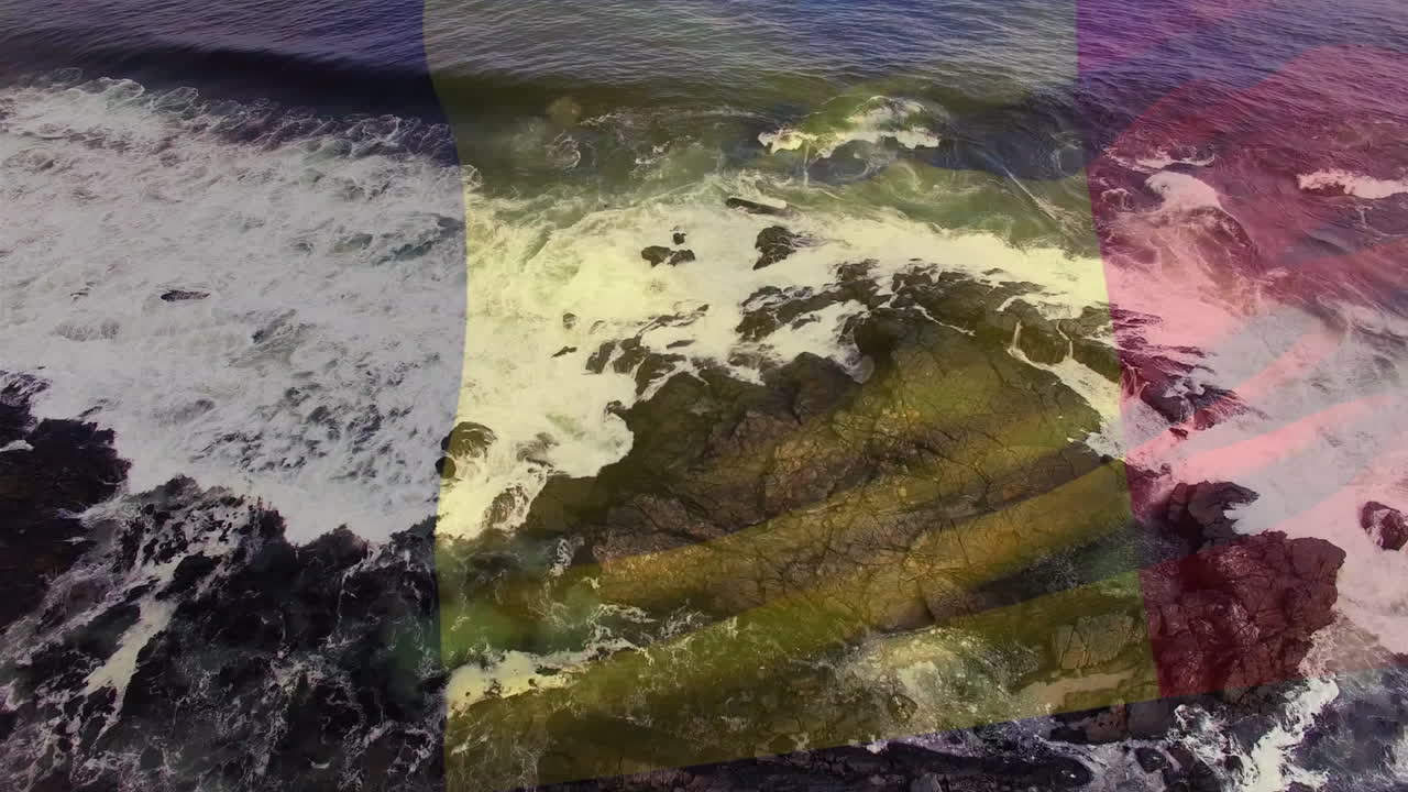 composición digital de ondear la bandera de bélgica contra las olas del mar que golpean las rocas