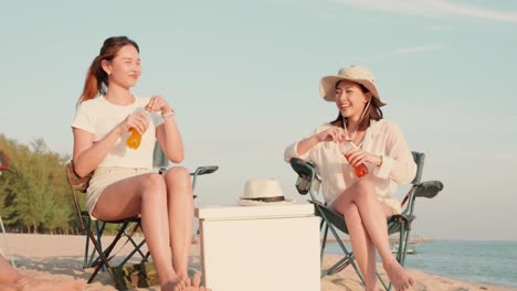 happy friends with drinks in camp and laughing together in holidays on sand beach near camping tent vacation time at sunset