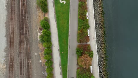 Top-down-aerial-view-of-the-Elliott-Bay-Trail-with-the-ocean-and-train-tracks-on-either-side,-Seattle