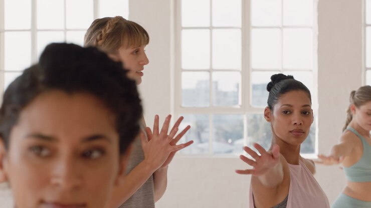 yoga class instructor teaching warrior pose to beautiful group of women enjoying healthy lifestyle exercising in fitness studio meditation