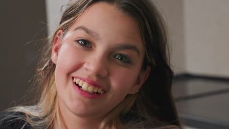 close up of young woman with black top smiling and looking at camera, natural expression, indoor setting, warm lighting, casual mood, youthful and friendly appearance, focused on face and eyes