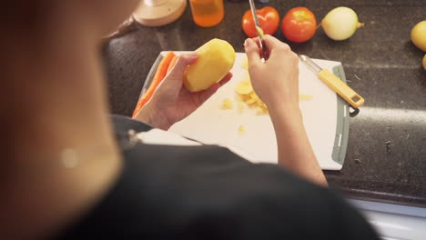 manos femeninas pelando papas en la tabla de cortar de la cocina