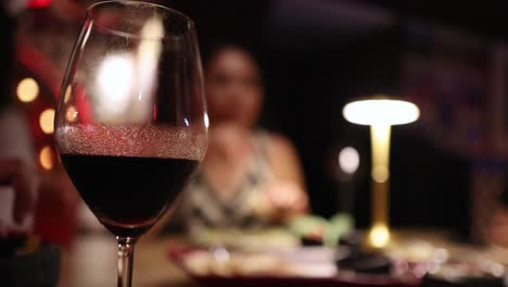a close-up of a red wine glass being gently swirled on a dinner table with dim, warm lighting and a blurred restaurant background