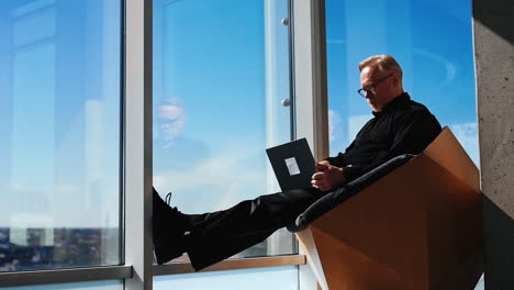 adult man sits in designer chair holding a laptop on his laps. man works remote or freelance in a comfortable place. low angle view.