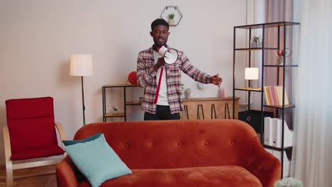 Young-man-shout-in-megaphone-loudspeaker-announces-discounts-sale-of-real-estate-at-home-on-sofa