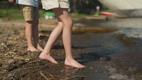 brother and sister with bare feet going into water ready to relax and enjoy swimming. holiday with family by sea. checking water temperature with body parts