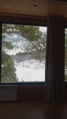 big panoramic window of resort cottage house with view of scenic mountains and coniferous trees covered with snow. winter landscape in gorny altai region