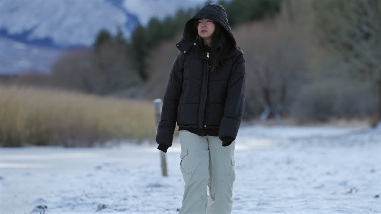 Woman walking through alone on the frozen lake shore in winter nature landscape