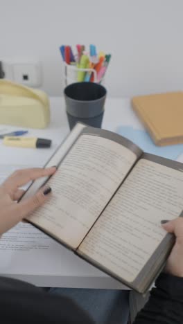 person opening and reading a book on a desk