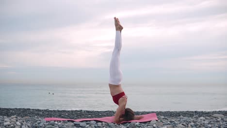 mujer practicando yoga de pie en la cabeza en una playa